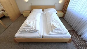 Ein Doppelbett mit weißen Leinen und Handtüchern, ein hölzerner Kopfteil, Nachttische und ein Fenster mit Vorhängen.