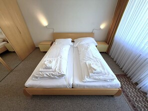 A double bed with white linens and towels, a wooden headboard, bedside tables, and a window with curtains. - Apollo 44 # 4-bed apartment, Bad, WC 4-Bettwohnung, Bad, WC by Interhome (Leukerbad)