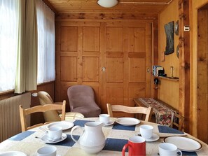 A wooden interior with a dining table set for four, chairs, a radiator, and a shelf with books and a kettle. - Chalet Willi-1.OG Appartement/Fewo, Dusche und Bad, WC, 9-Bettwohnung by Interhome (Arosa)