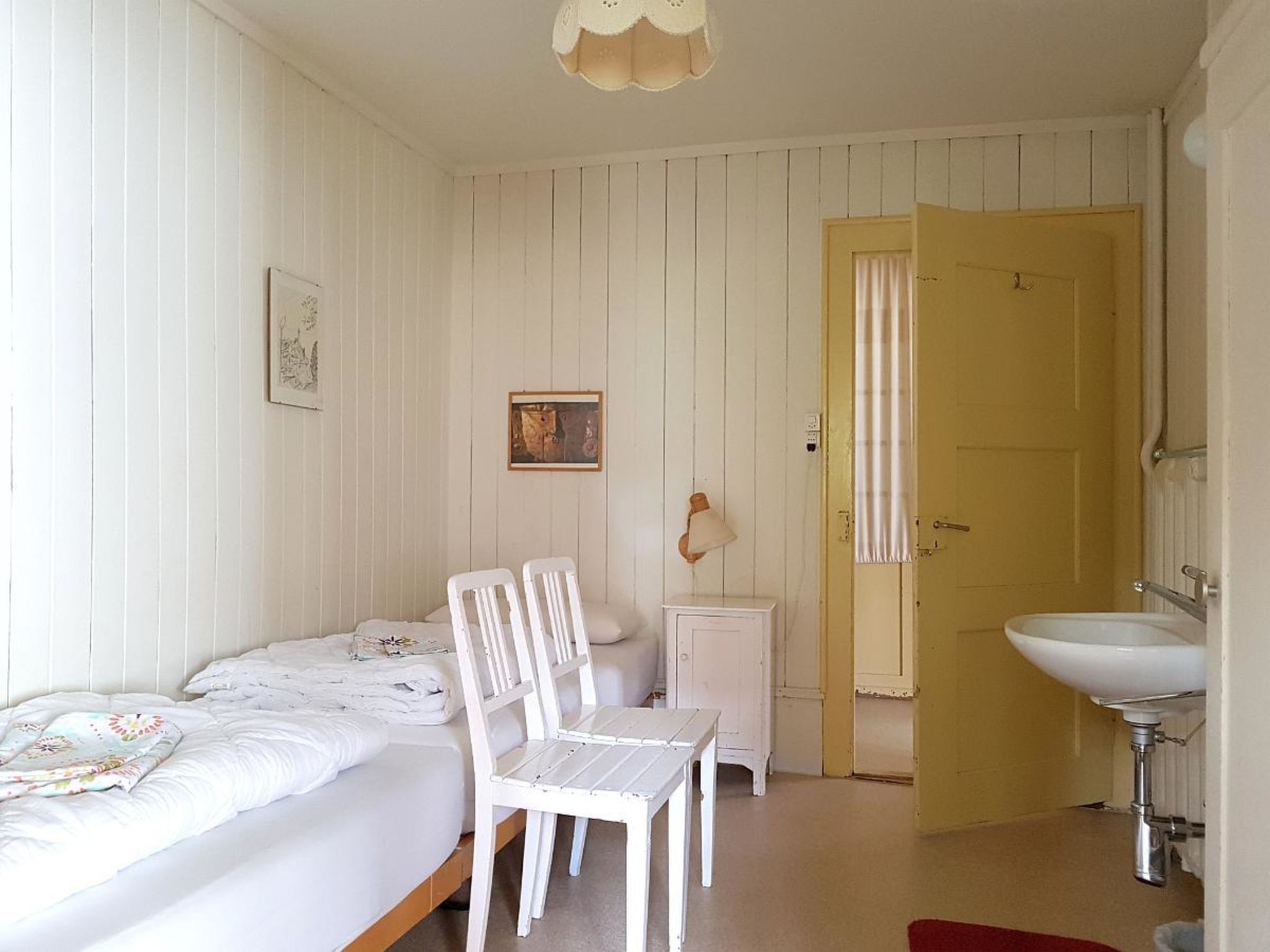 A room with a bed, a chair, a small table, a door, and a sink.