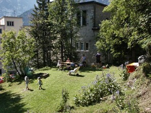 A residential area with a stone building, a grassy yard, and a few people. - Chalet Willi-1.OG Appartement/Fewo, Dusche und Bad, WC, 9-Bettwohnung by Interhome (Arosa)