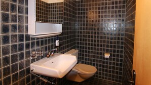 Ein Badezimmer mit Waschbecken, Spiegel, Toilette und dunkel gefliesten Wänden.