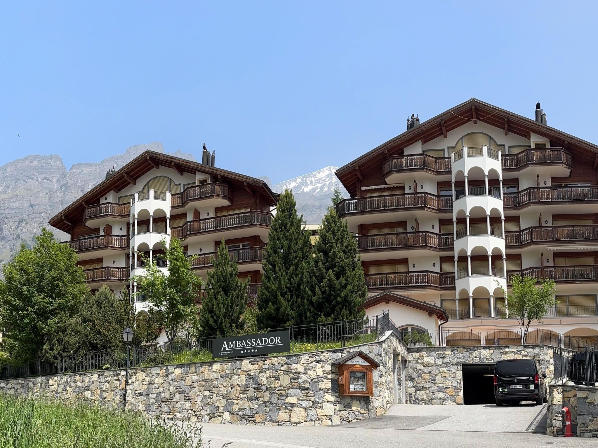 A hotel with multiple balconies, a stone wall entrance, and a mountain backdrop.