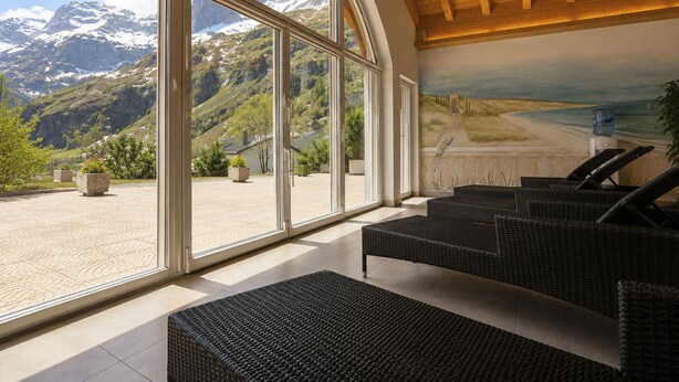A room with large windows offering a mountain view, wicker furniture, and a ceiling with wooden beams. - Ambassador Leukerbad # 4-bed apartment, Dusche und Bad, WC by Interhome (Leukerbad)