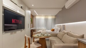 A modern hotel room with a large flat-screen TV displaying the Netflix logo, a cozy seating area with a sofa and a dining table set for two, and a small kitchenette. - Film studio with parking space - 800 m from the park. Ibirapuera (São Paulo)