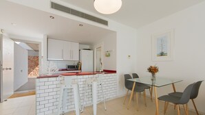 A modern kitchen with white cabinets, a microwave, and a red countertop. There is a dining area with a glass table and four chairs.