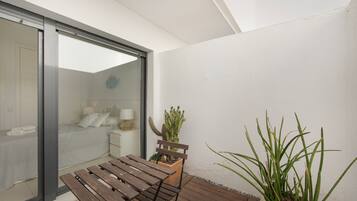Una terraza de madera con un banco, un cactus en maceta y una planta alta de hojas largas.