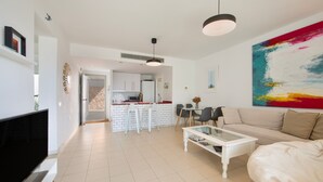 A modern living room with a flat-screen TV, a white sofa, and a glass coffee table.