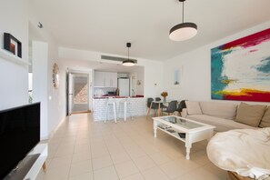 Una sala de estar moderna con un televisor de pantalla plana, un sofá blanco y una mesa de centro de vidrio.