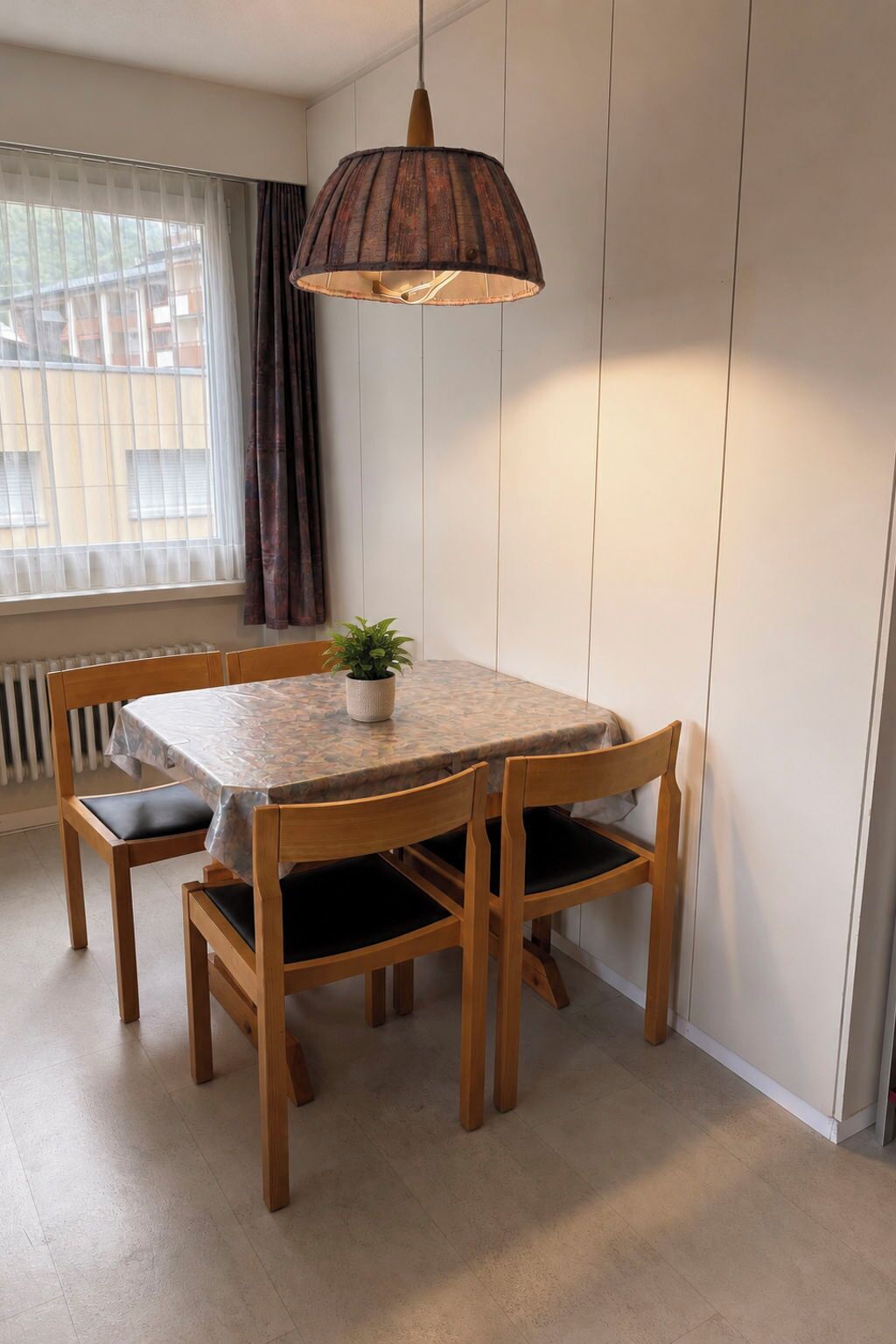 Un coin repas comprenant une table et des chaises, un luminaire suspendu, une fenêtre avec des rideaux et un radiateur.
