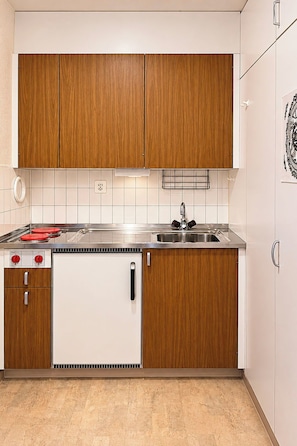 Eine kleine Küche mit Holzausbau, einem Edelstahlspülbecken und einem eingebauten Backofen.