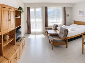 A hotel room with a bed, two chairs, a wooden cabinet, and a window with curtains. - Residenz Siesta Leukerbad # 5-bed apartment, Bad, WC by Interhome (Leukerbad)