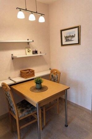 Ein Essbereich mit Holztisch, zwei Stühlen, einer Hängeleuchte und einem gerahmten Bild an der Wand.