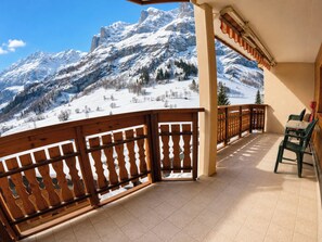 Ein Balkon mit Blick auf schneebedeckte Berge, Holzgeländern und einem Tisch mit Stühlen.