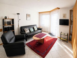 Ein Wohnzimmer mit einer schwarzen Ledersofa, einem Couchtisch, einem roten Teppich, einem Fernseher und einem Bücherregal.