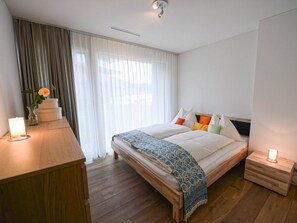 Een moderne slaapkamer met een houten bed, een nachtkastje, een dressoir en een raam met gordijnen.