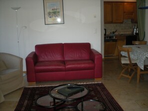 Ein Wohnzimmer mit einem roten Sofa, einem kleinen Couchtisch und einem Essbereich mit Tisch und Stühlen.