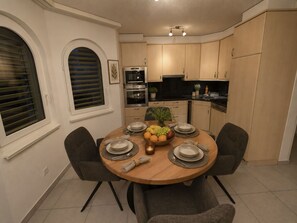 A dining area with a round table set for four, surrounded by chairs. There is a kitchen area with cabinets and appliances in the background. - Ambassador A11 # 4-bed apartment, Dusche und Bad, WC by Interhome (Leukerbad)