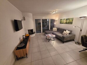 Uma sala de estar com sofá, mesa de centro, televisão e lareira.