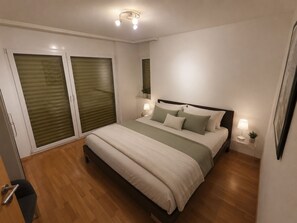 Une chambre à coucher avec un lit, des lampes de chevet, une fenêtre avec des stores et une porte.