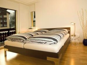A modern bedroom with a large bed, a bedside table, a lamp, and a view of the outside. - Ambassador A11 # 4-bed apartment, Dusche und Bad, WC by Interhome (Leukerbad)