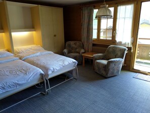 Hotelkamer met twee bedden, een stoel, een tafeltje en een raam met gordijnen.
