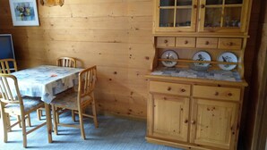 Un interior de madera con una mesa de comedor, sillas, una lámpara colgante y una zona de cocina con armarios y encimera.