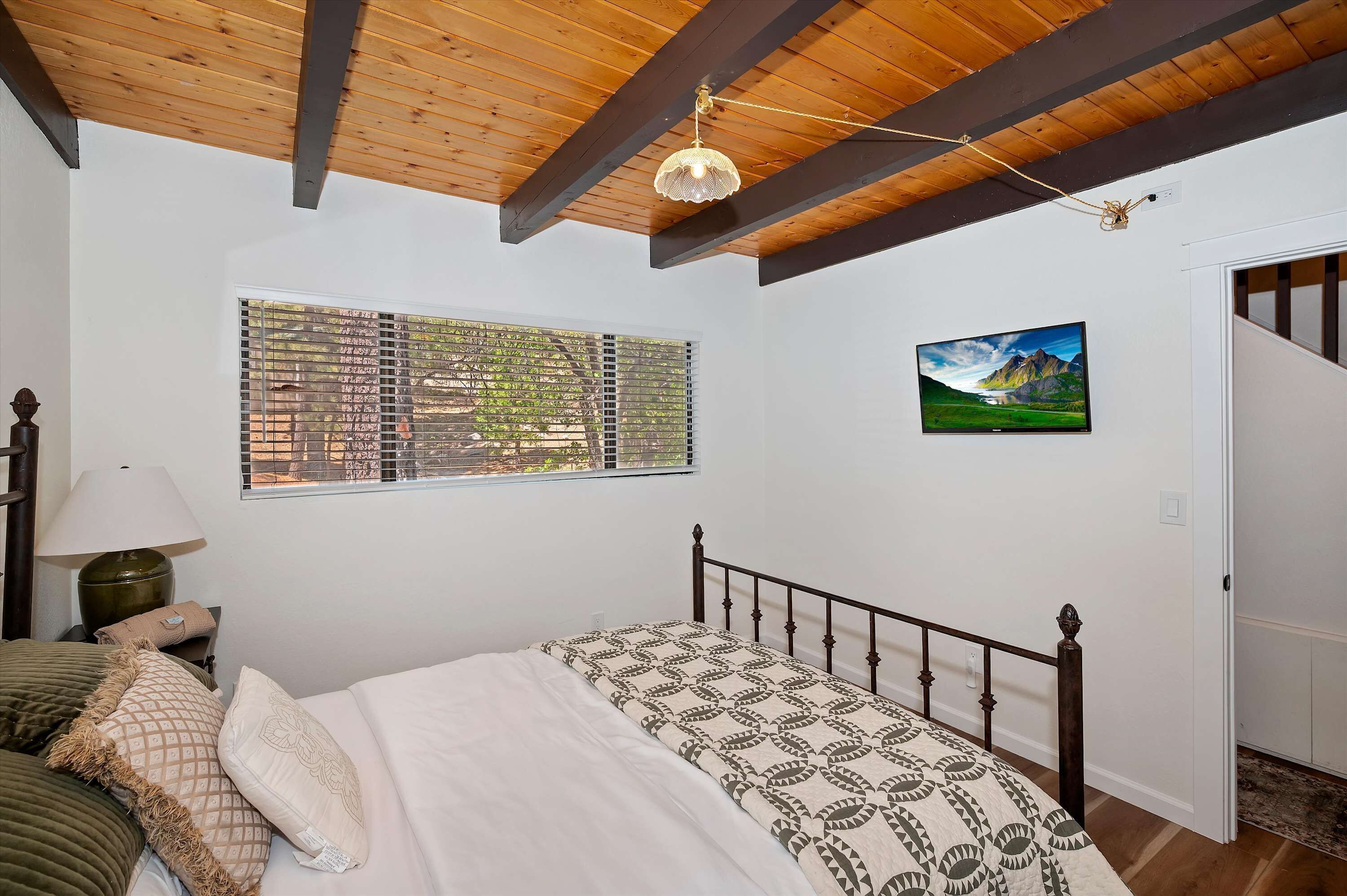 Ein Schlafzimmer mit Holzboden, einem Bett mit gemusterten Betttextilien, einem Fenster mit Jalousien, einer Lampe und einem Bild an der Wand.