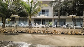 A beachfront hotel with white lounge chairs, palm trees, and umbrellas.