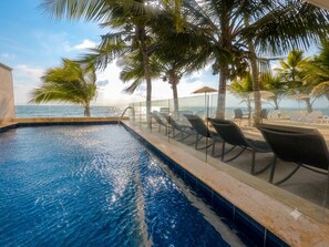 A swimming pool with lounge chairs and umbrellas, overlooking a beach.