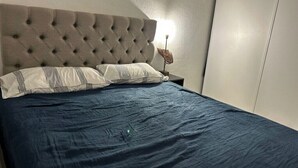 A bedroom with a tufted headboard, a bed with a dark blue bedspread, two pillows, and a bedside table with a lamp. - House with a garden in Candillargues (Candillargues)