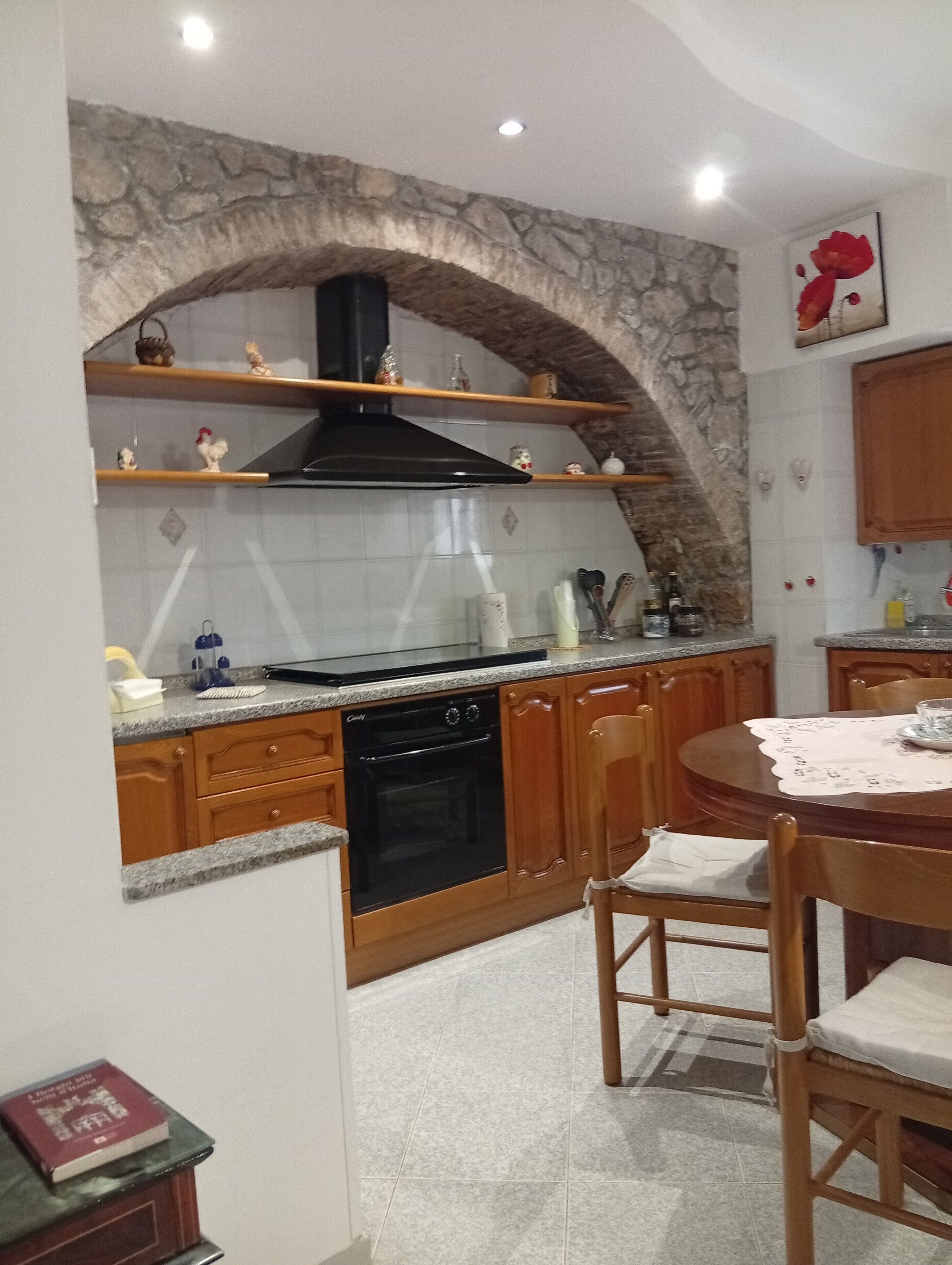 Una cocina con arco de piedra, armarios de madera, un horno negro y una mesa de comedor con sillas.