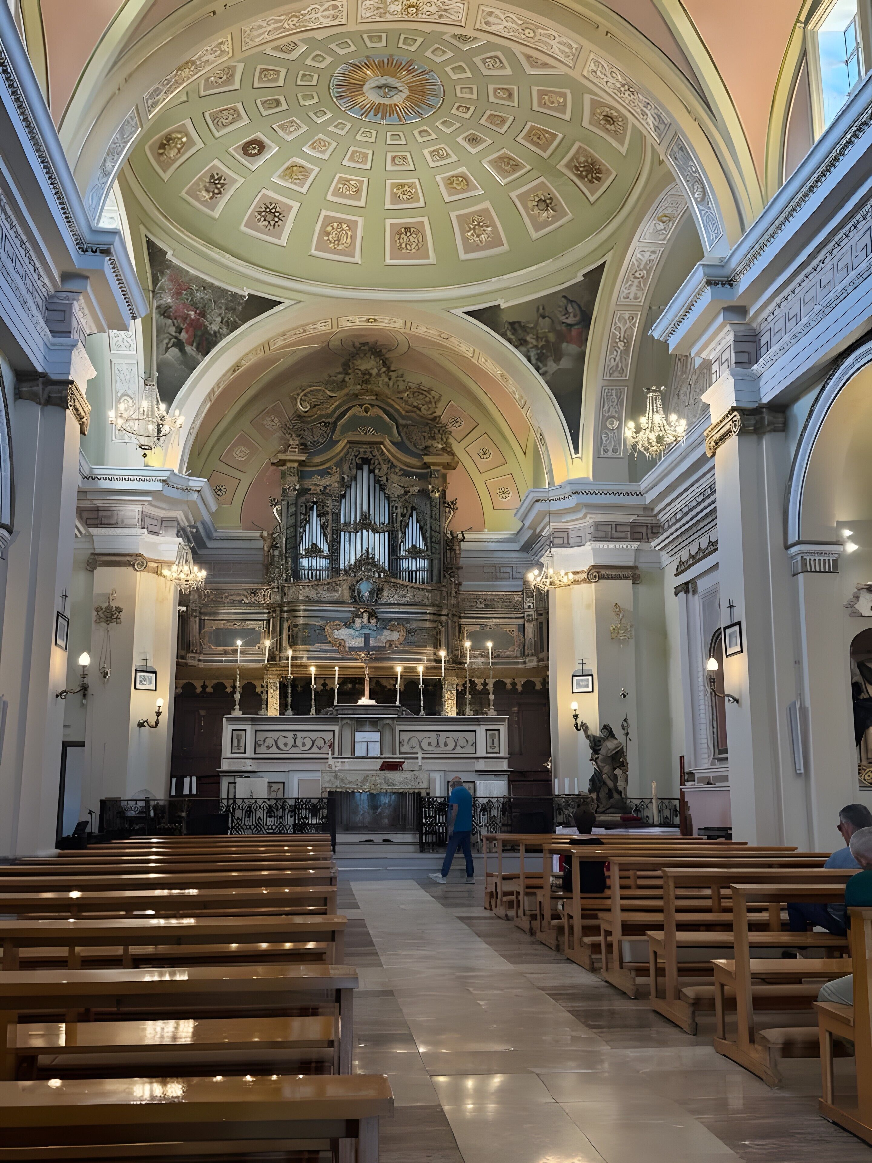 En kyrkinteriör med bänkar, en stor orgel och utsmyckade takdekorationer.