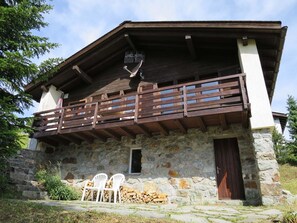 Ein rustikales Steinhaus mit Holzbalkon, einer Tür und zwei weißen Stühlen vor der Fassade.
