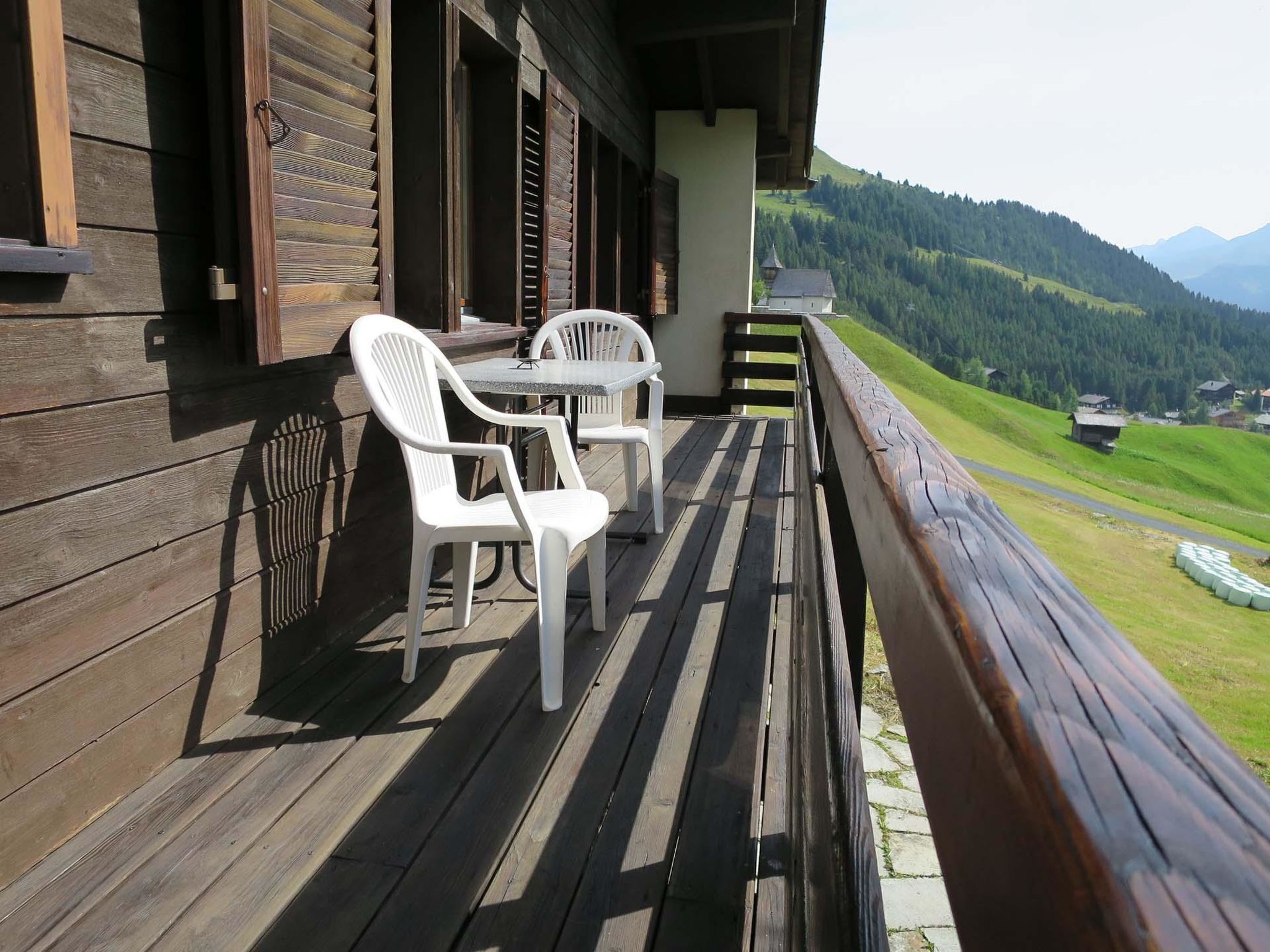 A wooden deck with two white plastic chairs and a table, overlooking a mountainous landscape.