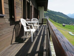 Eine Holzterrasse mit zwei weißen Plastikstühlen und einem Tisch, mit Blick auf eine gebirgige Landschaft.