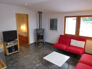 Ein Wohnzimmer mit Fernseher, einem roten Sofa, einem weißen Couchtisch, einem Kamin und einem Fenster.