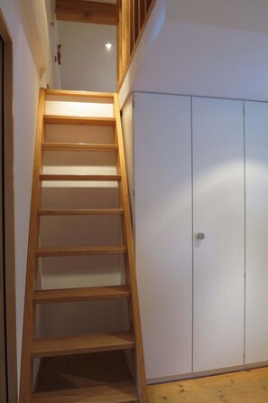 Eine Holztreppe führt zu einer Zwischenebene mit einem weißen Schrank und einer Tür.