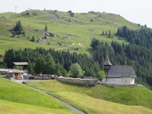 Ländliche Umgebung mit einem Steinhaus, einer Holzhütte mit spitzer Dachform und einem Pfad, der bergauf führt.