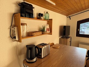 A kitchenette with a coffee maker, toaster, kettle, and a shelf with various items including a book and spices. - Village Center Studio – Ski-in/Ski-out (La Clusaz)