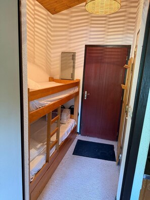 A narrow room with bunk beds, a wooden door, and a small heater on the wall. - Village Center Studio – Ski-in/Ski-out (La Clusaz)