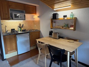 A compact kitchen with wooden cabinets, a microwave, a coffee maker, and a toaster on a wooden table. - Village Center Studio – Ski-in/Ski-out (La Clusaz)
