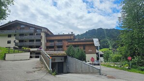 Ein mehrstöckiges Gebäude mit Balkonen, einem Parkplatz und einer Bergkulisse.