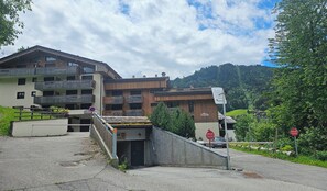 A multi-story building with balconies, a parking area, and a mountainous backdrop. - Village Center Studio – Ski-in/Ski-out (La Clusaz)