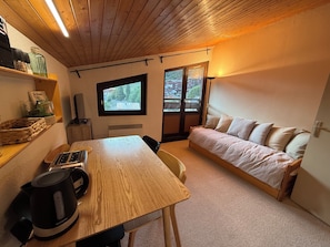 A cozy room with a wooden table, a sofa, a window, and a radiator. - Village Center Studio – Ski-in/Ski-out (La Clusaz)