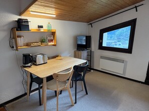 A compact kitchen with a wooden table, two chairs, a kettle, a toaster, and a television.