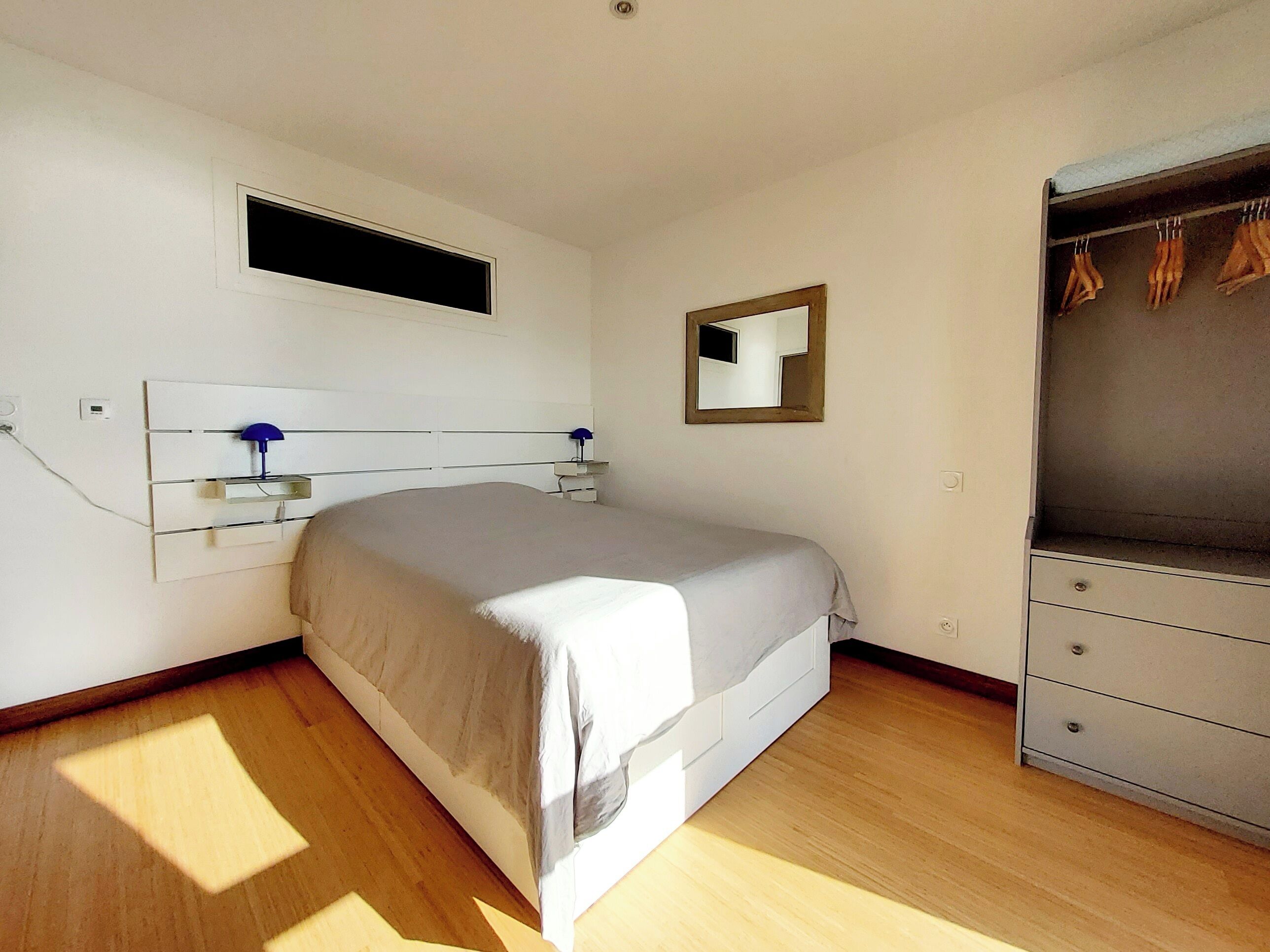 Une chambre à coucher avec un lit, une armoire, un miroir et une fenêtre.