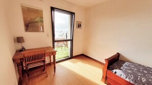 A room with a wooden desk, a bed, a window, and a framed picture on the wall.