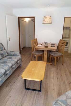 Un espace de vie compact comprenant une table à manger pour quatre personnes, entourée de chaises en bois. Un canapé est placé à gauche, et une petite table en bois se trouve au premier plan.