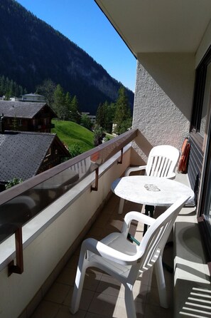 Ein Balkon mit Tisch und Stühlen, mit Blick auf eine gebirgige Landschaft.